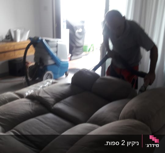 אדם מנקה ספה עם שואב אבק מקצועי